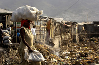 A woman carries grapefruits across a trench of garbage at a market near La Saline.