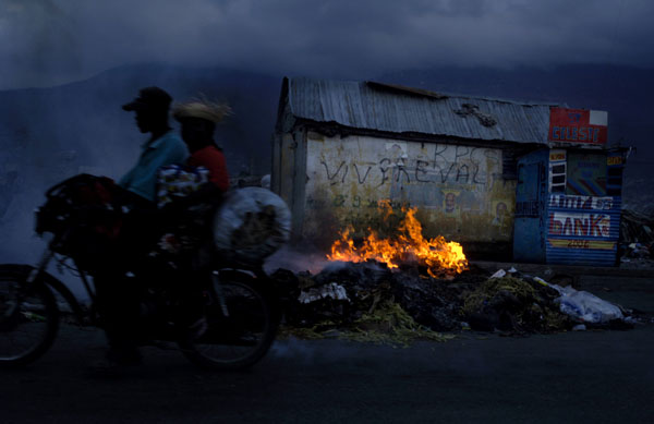 Garbage burns at dusk in front of a shack painted with Preval slogans at a market near La Saline. : Haiti 2006 : Jason DeCrow Photojournalist