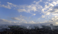 A lone woman wanders through vast fields of burning garbage searching for items to salvage on the outskirts of Port-au-Prince.